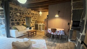A cozy living room with a stone wall, wooden ceiling, and a dining area with a table and chairs. - The House of Small Things (Lascelle)