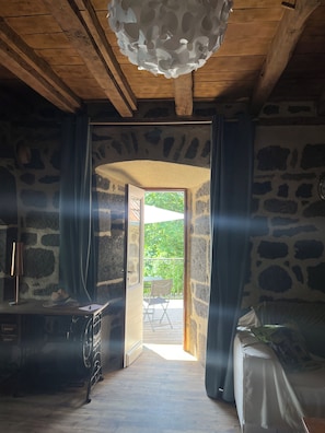 Une chambre rustique avec des murs en pierre, des poutres en bois, un lit, un bureau et une vue sur un patio extérieur.