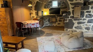 A stone-walled room with a dining table, chairs, a sofa, and a television. - The House of Small Things (Lascelle)
