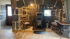 A rustic stone fireplace with a modern wood-burning stove, a wooden chair, and a metal cart with baskets. - The House of Small Things (Lascelle)