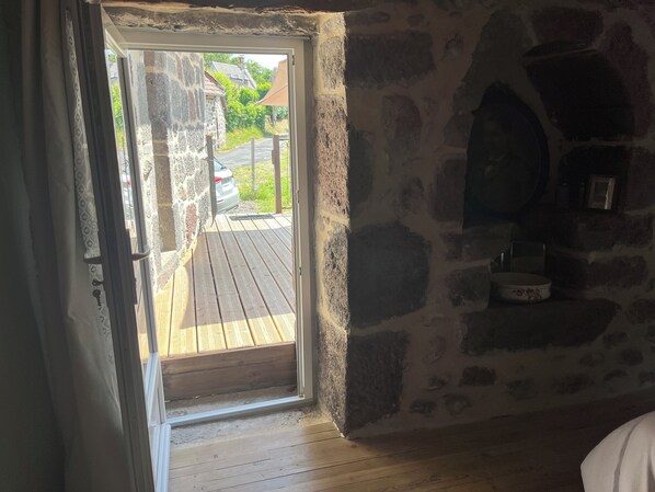 Une pièce avec un mur en pierre, un plancher en bois, une porte donnant sur l’extérieur et une petite étagère sur laquelle sont posés divers objets.