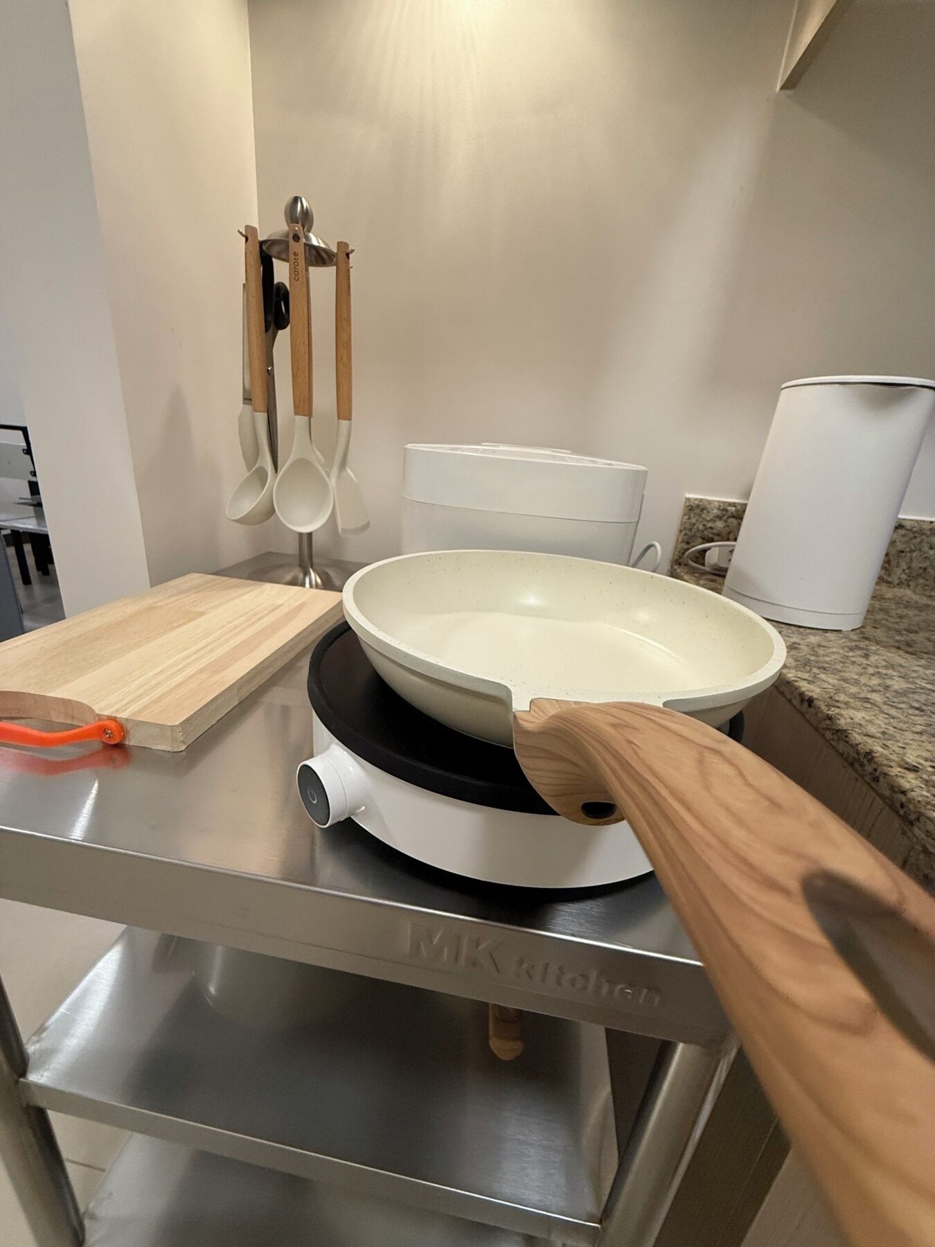 Eine Küche mit einem weißen Induktionskochfeld, einem Holzschneidebrett und einer weißen Schüssel auf der Arbeitsfläche.