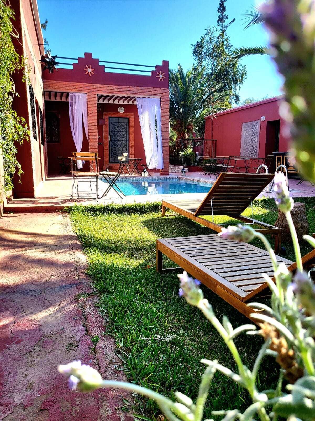 A pool area with lounge chairs, a small building with a red exterior, and a clear blue sky.