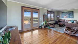 A spacious living room with a wooden floor, a leather sofa, a coffee table, and a large window with a view of the outdoors. - Rustic country lodge with spectacular fire pit and nearby hiking trails (Hallston)