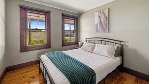 A bedroom with a bed, two windows, a nightstand, and a painting on the wall. - Rustic country lodge with spectacular fire pit and nearby hiking trails (Hallston)