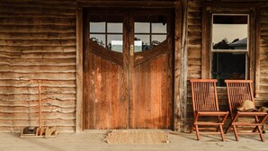 A rustic wooden cabin with a large wooden door, two wooden chairs, and a small rug on the porch. - Rustic country lodge with spectacular fire pit and nearby hiking trails (Hallston)