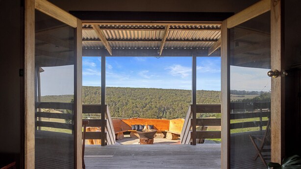 An open wooden door leading to a deck with a fire pit and a view of a forested hill. - Rustic country lodge with spectacular fire pit and nearby hiking trails (Hallston)