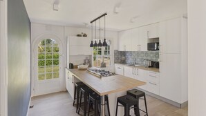 Une cuisine moderne dotée d’un grand îlot central, de tabourets de bar et offrant une vue sur la verdure environnante.