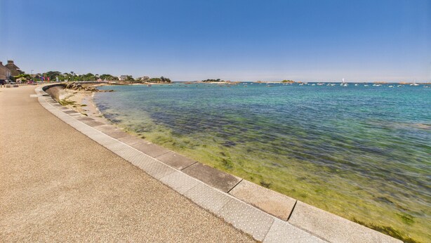 Une promenade en bord de mer, avec une eau claire, une barrière en pierre et des bâtiments en arrière-plan.