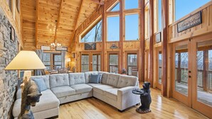 A large wooden interior with a sectional sofa, a bear statue, and a sign reading "Welcome to our Neck of the Woods."