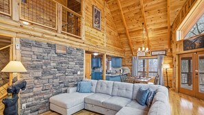 A cozy log cabin interior with a stone wall, a gray sectional sofa, and a bear statue.