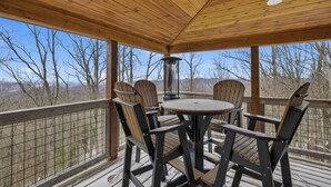A wooden deck with a round table and four chairs, overlooking a mountainous landscape.