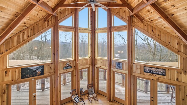 A wooden cabin with a high ceiling and large windows. There are two wooden chairs on the deck.