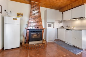 Eine Küche mit Kamin aus Backsteinen, weißen Schränken, einem weißen Kühlschrank und einer Mikrowelle.