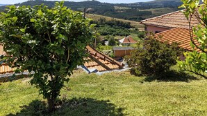 Paisaje rural con una casa, un árbol y colinas onduladas al fondo.