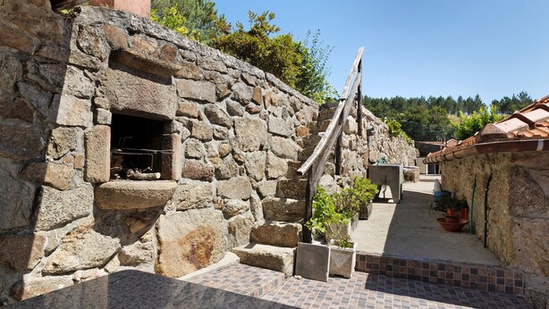 Un edificio de piedra con chimenea, escalones que conducen a una zona con baldosas y plantas en macetas.