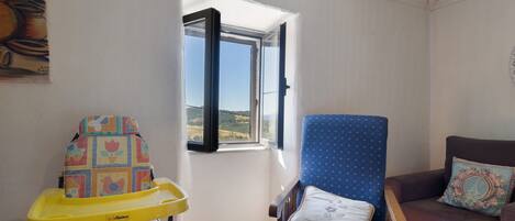 A room with a window, a blue chair, a sofa, and a child's high chair.