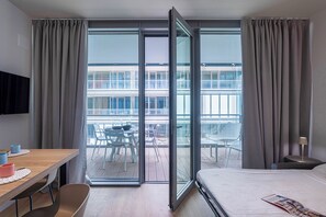 A hotel room with a bed, a desk, and a balcony with chairs and a table. - Waterfront Blue by Wonderful Italy (Genoa)