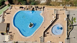 An aerial view of a swimming pool with a heart-shaped design, a smaller circular pool, and surrounding walkways.