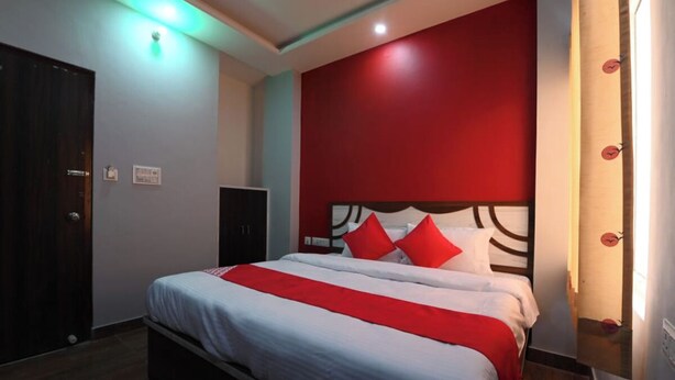 Habitación de hotel con cama, pared de acento roja, puerta de madera y un mueble pequeño.