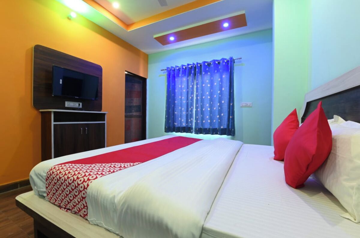 A hotel room with a bed, a TV mounted on the wall, a wardrobe, and a window with blue curtains.