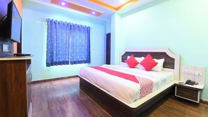 Habitación de hotel con cama, escritorio, televisión y ventana con cortinas.