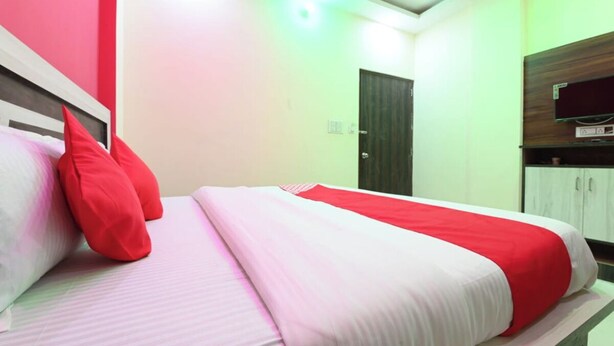 Habitación de hotel con cama, almohadas rojas, colcha blanca y roja, armario de madera y televisor en la pared.