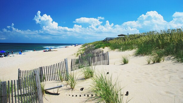 A beach with a wooden fence, beachgoers, and a lifeguard tower. - Casa de Playa 4 Bedroom Home in Kill Devil Hills (Kill Devil Hills)