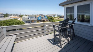 A wooden deck with a view of houses, a chair, and a window. - Casa de Playa 4 Bedroom Home in Kill Devil Hills (Kill Devil Hills)