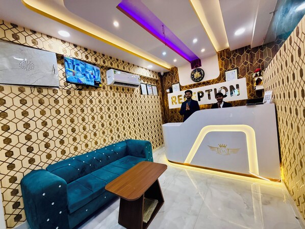 A reception area with a sofa, a reception desk, and a wall-mounted TV. - Hotel Golden Crystal (Patna)