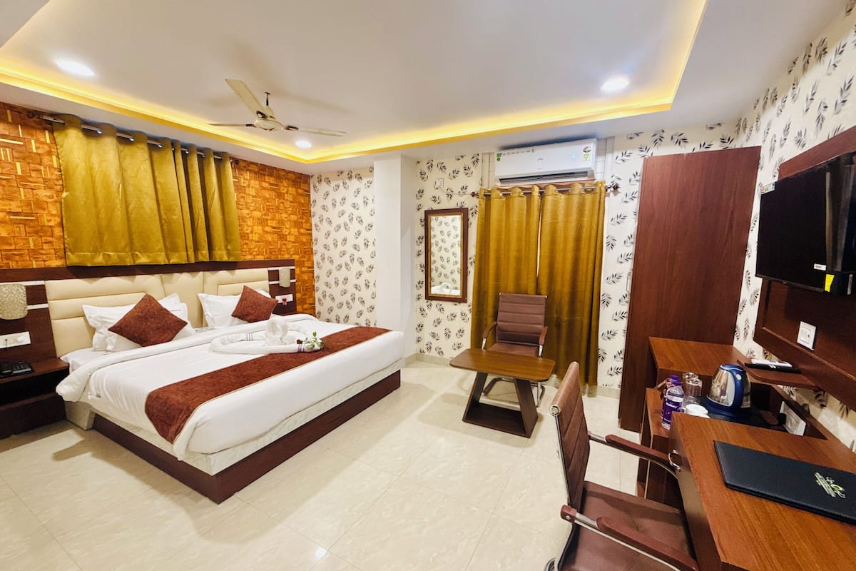 Quarto de hotel com cama, escrivaninha, cadeira, televisão e ar condicionado.