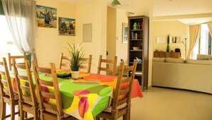 A dining area with a colorful tablecloth, wooden chairs, a potted plant, and a bookshelf. - BELLEVUE VILLA. Completely private 3-bedroom villa with pool, gardens & orchard. (Anarita)