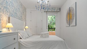 A bedroom with a bed, two bedside lamps, a dresser, a chandelier, a window with a view, and a piece of abstract art on the wall. - Apartment 'Casa Alicate' with Shared Pool, Wi-Fi and Air Conditioning (Marbella)