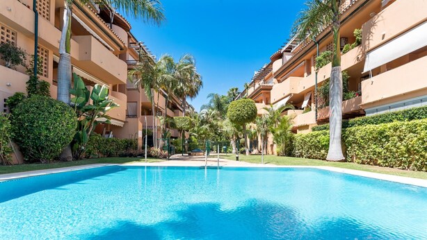 A swimming pool surrounded by multi-story buildings with balconies, palm trees, and well-maintained greenery. - Apartment 'Casa Alicate' with Shared Pool, Wi-Fi and Air Conditioning (Marbella)