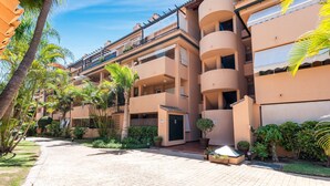 A multi-story hotel with balconies, a paved courtyard, and tropical landscaping. - Apartment 'Casa Alicate' with Shared Pool, Wi-Fi and Air Conditioning (Marbella)