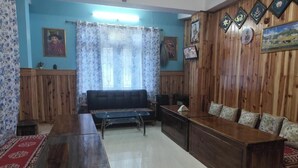 A living room with a wooden sofa, a long wooden table, and a patterned rug. - Gyalpo Homestay (Tawang)