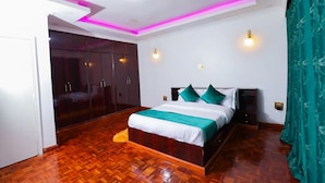 A bedroom with a wooden floor, a bed with white and teal bedding, a wardrobe, and pink ceiling lights. - Spacious & Beautiful 5-bedroom Villa in Nairobi with WiFi (Nairobi)