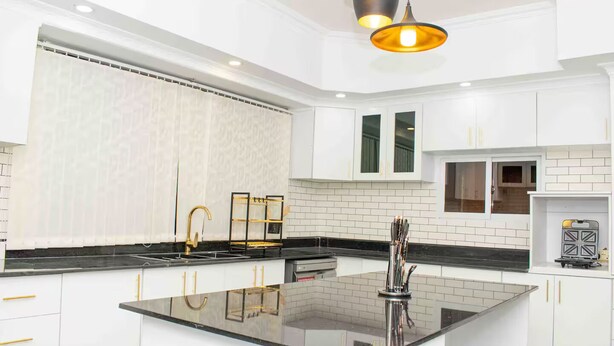 A modern kitchen with white cabinetry, a central island, and a black countertop. - Spacious & Beautiful 5-bedroom Villa in Nairobi with WiFi (Nairobi)