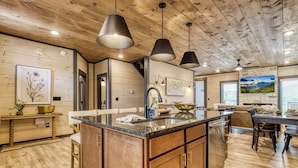 A spacious kitchen with a large island, wooden cabinets, pendant lighting, and a view of the dining area. - Carpenters Splashin Paradise -Free Waterpark, Theater Room, Private Pool! (Sevierville)