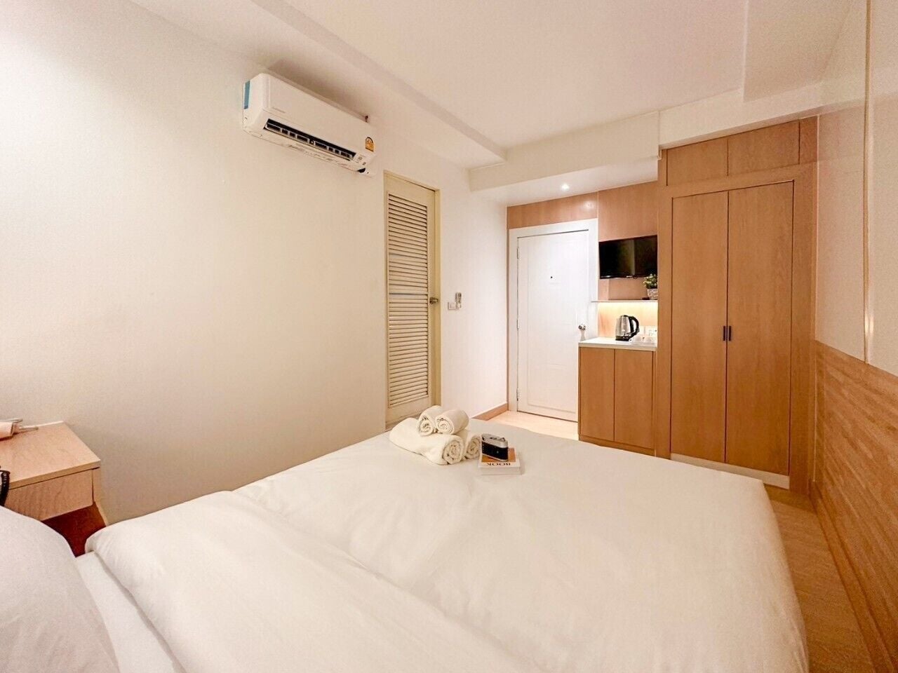 Ett hotellrum med en stor säng, ett sängbord, en luftkonditioneringsanläggning, en garderob och en liten köksdel.