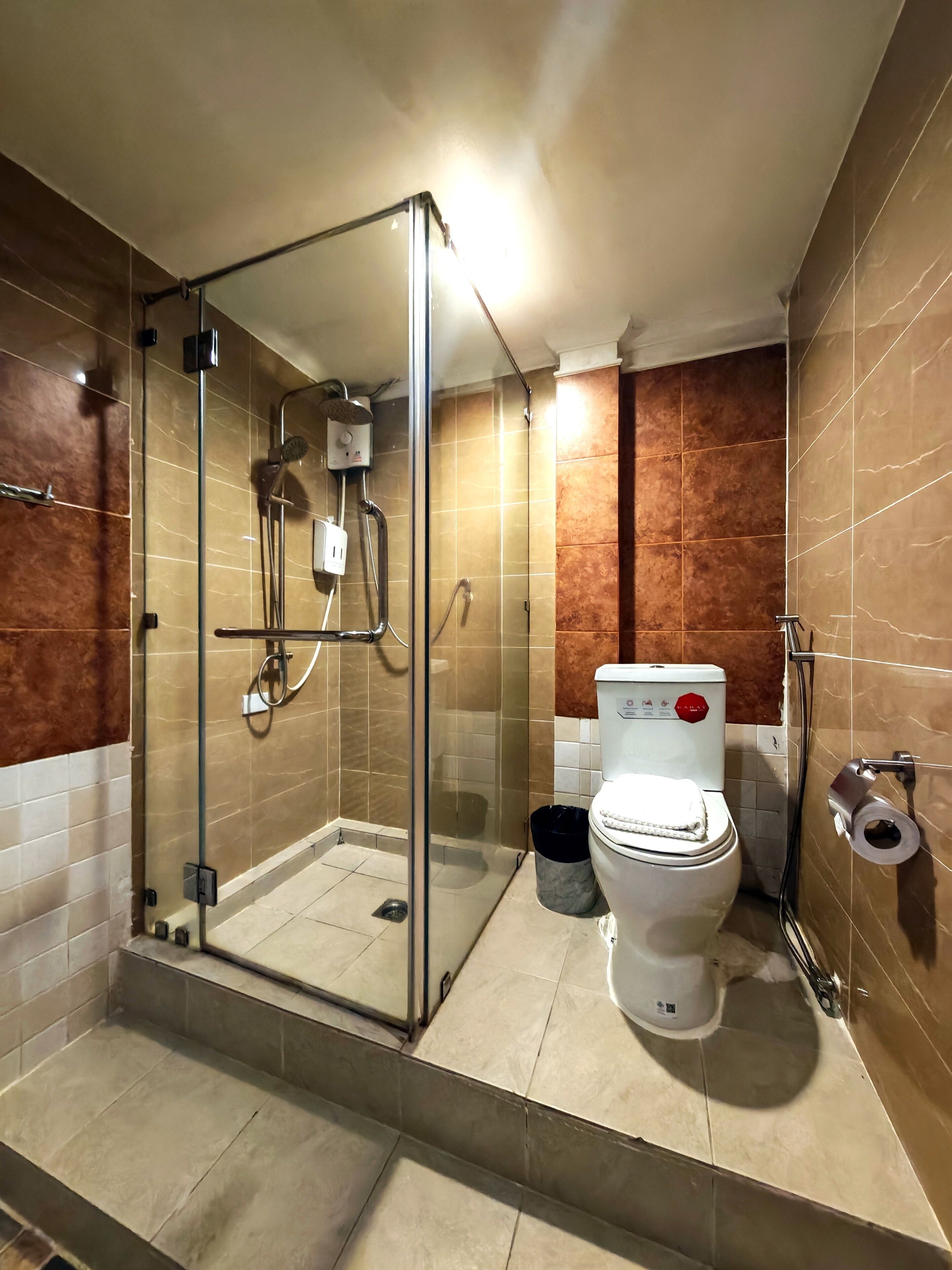 A modern bathroom with a glass-enclosed shower, a toilet with a red control panel, and a trash bin.