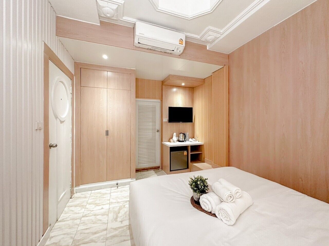 A modern hotel room with a large bed, a small bedside table, a TV, and a built-in wardrobe.