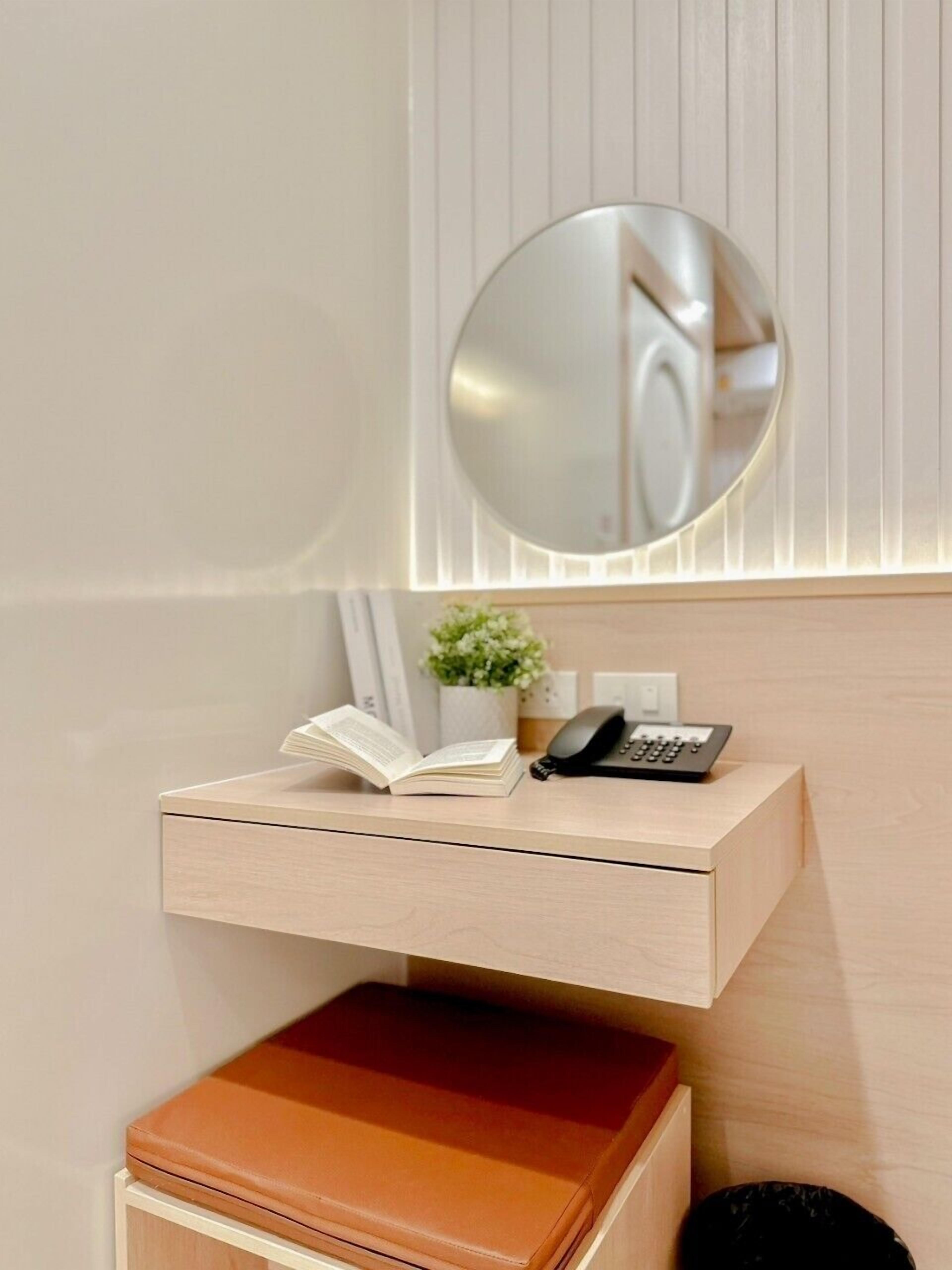 A modern bathroom with a wooden vanity, a round mirror, a small plant, and a book on the counter.