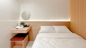 A hotel room with a bed, a bedside table with a lamp, a mirror, and a small plant. - Thrive Hotel (Bangkok)