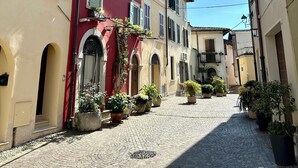 A cobblestone street lined with colorful buildings, featuring arched doorways and balconies with potted plants.
