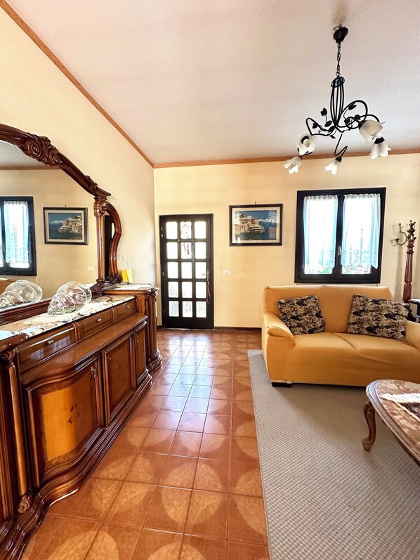 A living room with a sofa, a wooden cabinet, a mirror, and a chandelier.