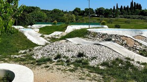 A landscaped area with pathways, a circular concrete feature, and a distant view of trees and a hill.