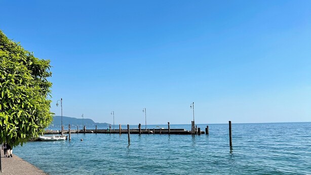A paved waterfront walkway with a clear view of the water and a distant pier.