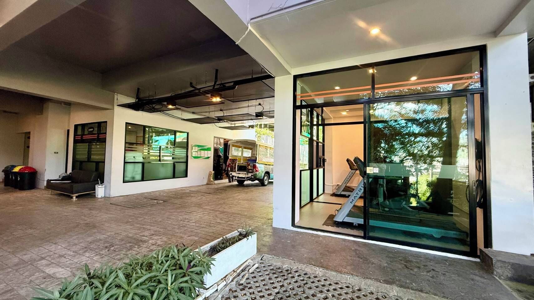A modern building with a covered outdoor area, a glass door entrance, and a treadmill inside.