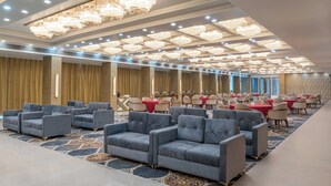 Une vaste salle de banquet avec des rangées de tables et de chaises, une moquette à motifs et un plafond orné de plusieurs lustres.